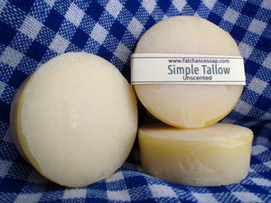 three bars of round, off-white tallow soap are stacked on a blue and white checked cloth