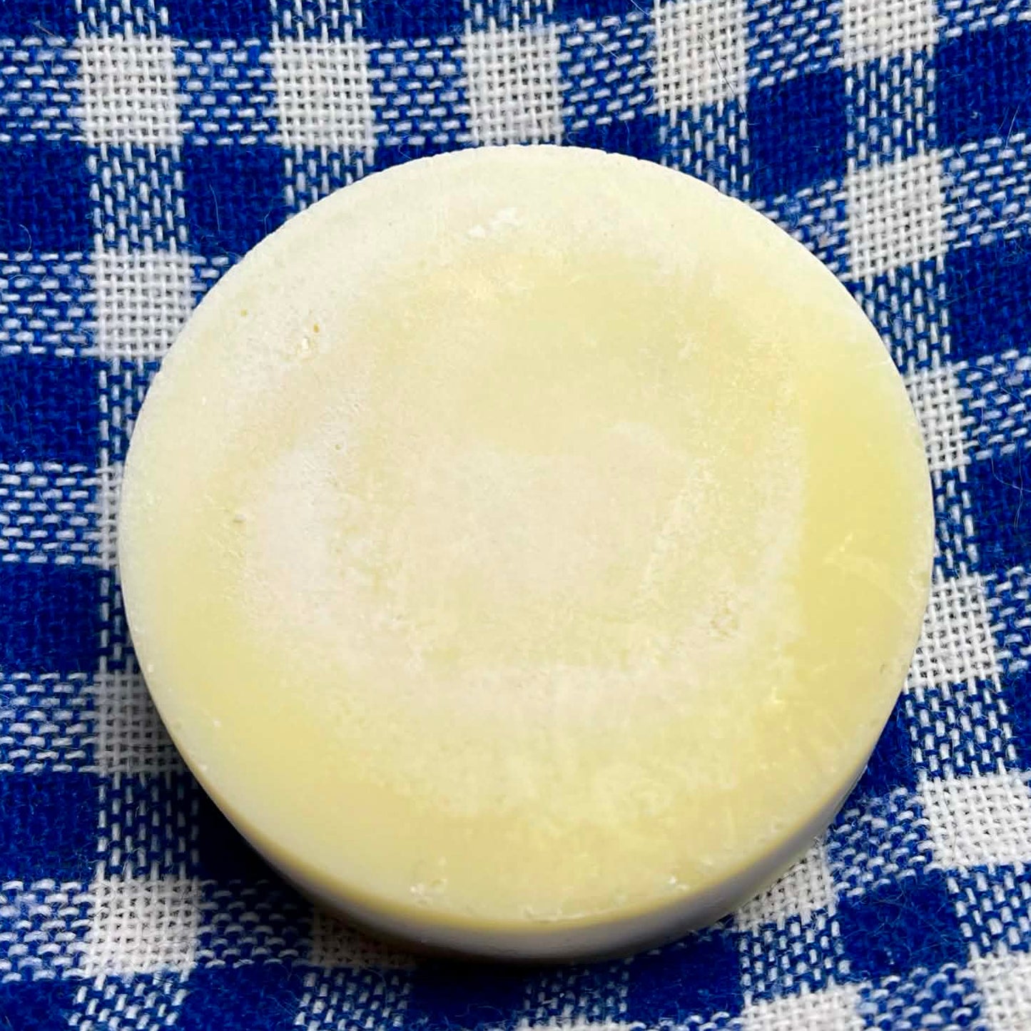 Round bar of soap on a blue and white checkered fabric background